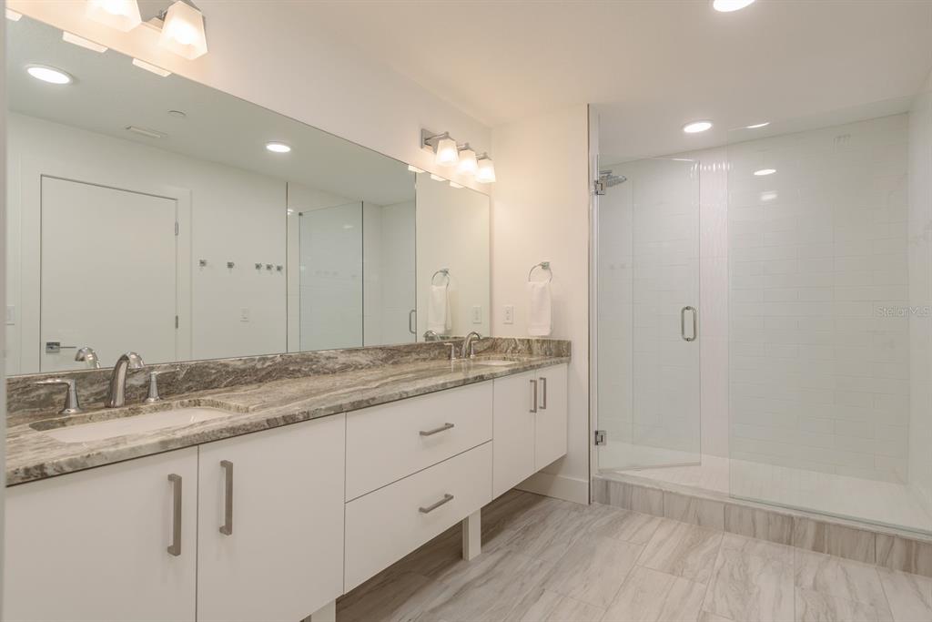 415 Island Way, Unit 402 Clearwater Beach, FL 33767 - Photo 23 of 35 a bathroom with a granite countertop sink a large mirror and a shower