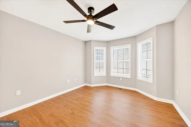 an empty room with wooden floor ceiling fan and windows
