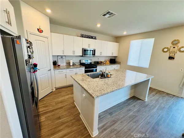 a kitchen with stainless steel appliances granite countertop a refrigerator a sink dishwasher a stove top oven a refrigerator and white cabinets with wooden floor