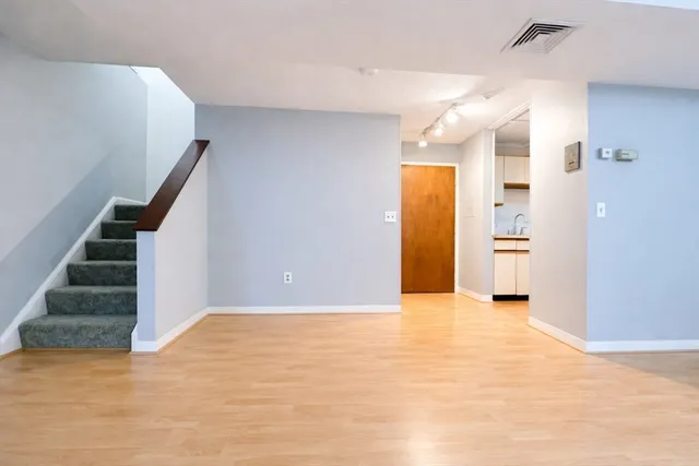 a view of an empty room with wooden floor and kitchen view