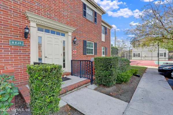 a view of a brick house with a yard plants and large tree