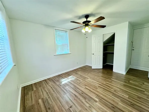 an empty room with wooden floor fan and windows