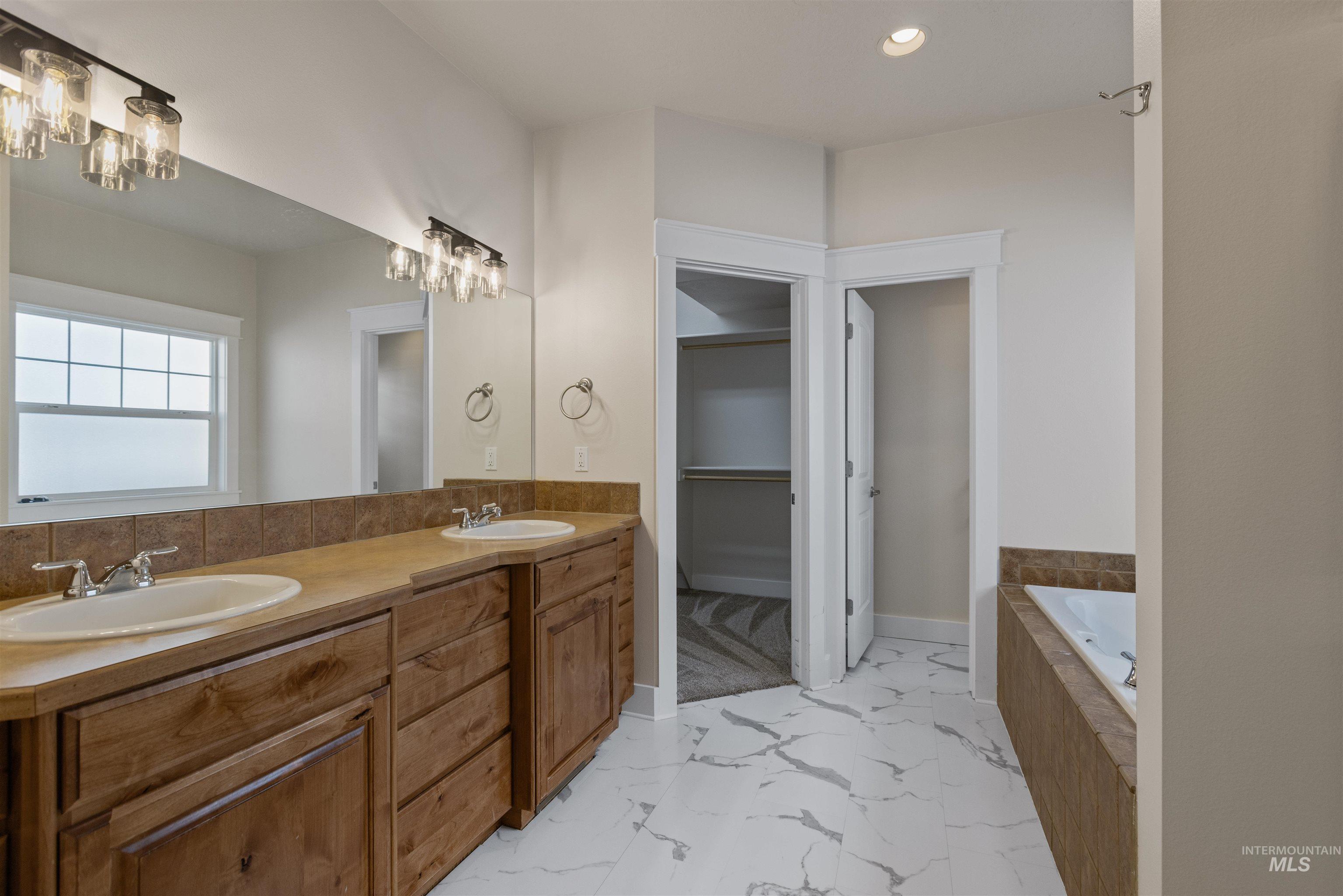 5426 West School Ridge Road Boise, ID 83714 - Photo 30 of 39 Dual vanity with wood-finish cabinetry and integrated sinks, oversized mirror, tile backsplash, built-in soaking tub, and walk-in closet with built-in shelving