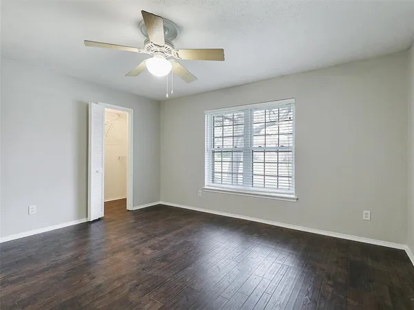 an empty room with wooden floor chandelier fan and windows