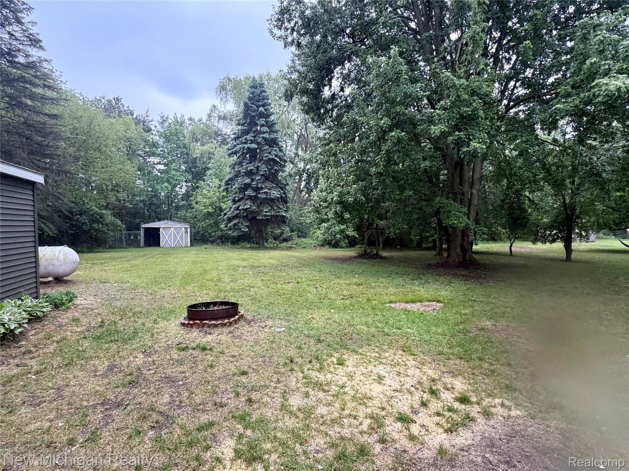 7104 Willard Road Millington, MI 48746 - Photo 29 of 30 Expansive backyard featuring mature trees, a detached storage shed, and a fire pit area