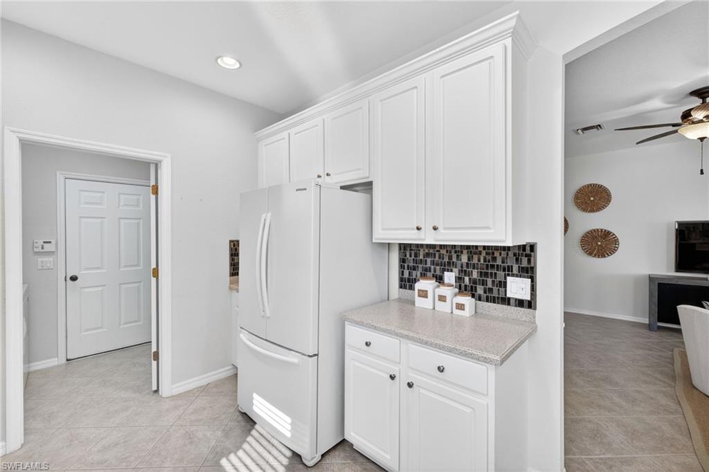 14088 Mirror Court Naples, FL 34114 - Photo 13 of 31 Kitchen featuring backsplash, white cabinetry, freestanding refrigerator and light tile patterned floors