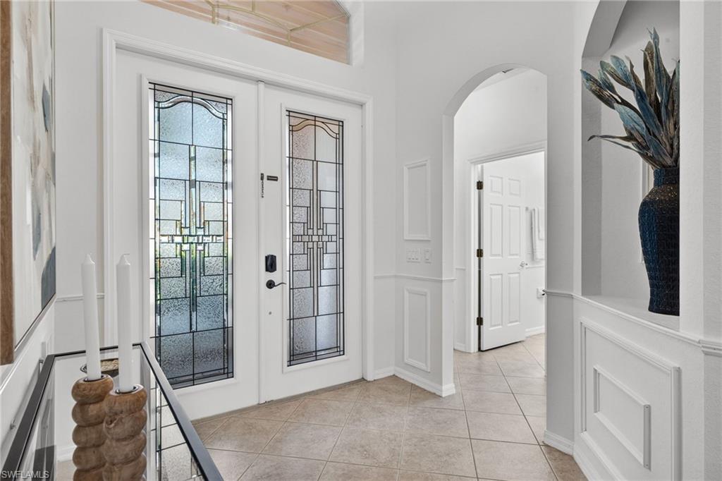 14088 Mirror Court Naples, FL 34114 - Photo 3 of 31 Foyer entrance featuring french doors, arched walkways, light tile patterned floors, a decorative wall niche, and a wainscoting