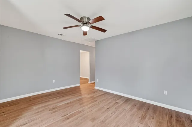 a view of an empty room with wooden floor and a ceiling fan