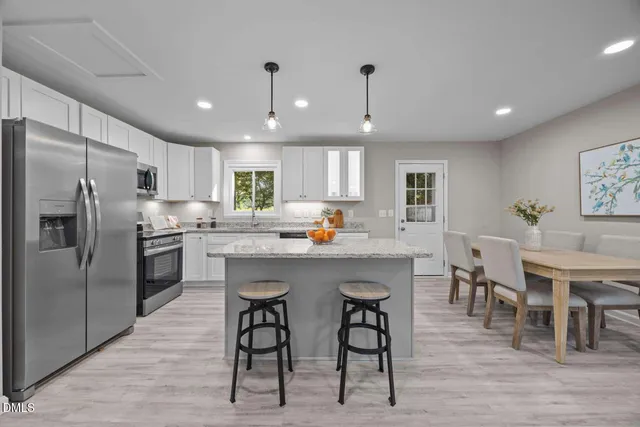 a kitchen with stainless steel appliances granite countertop a table chairs refrigerator and sink