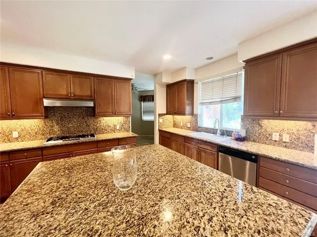 a view of a kitchen with kitchen island granite countertop a stove top oven a sink a counter space and cabinets