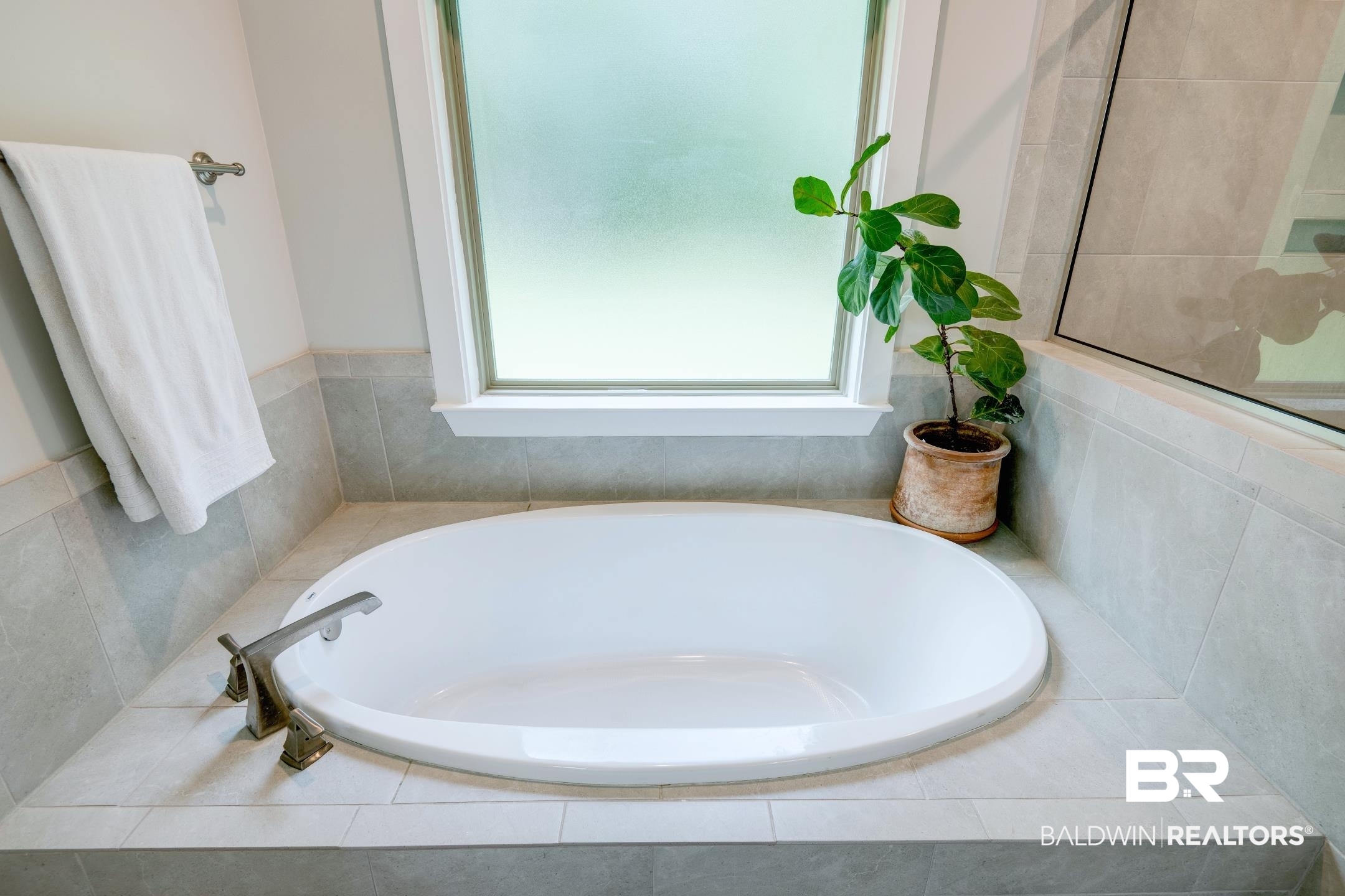 18754 Treasure Oaks Road Gulf Shores, AL 36542 - Photo 17 of 53 Built-in oval soaking tub with chrome fixtures, surrounded by light gray wall tiles and a frosted window