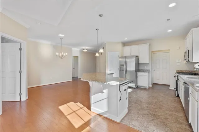 a open kitchen with stainless steel appliances granite countertop a refrigerator a stove a sink and a dining table with wooden floor