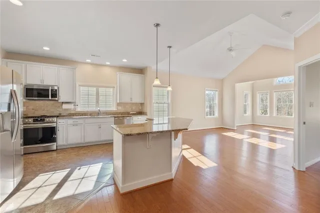 a kitchen with stainless steel appliances granite countertop a stove top oven a sink dishwasher a refrigerator and white cabinets with wooden floor