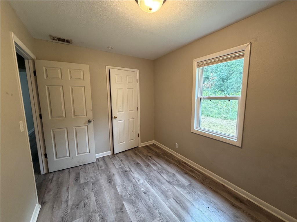 909 Riddell Street Clarksville, AR 72830 - Photo 21 of 26 Interior room featuring wood-finish flooring, neutral wall paint, white trim, and a double-hung window with blinds