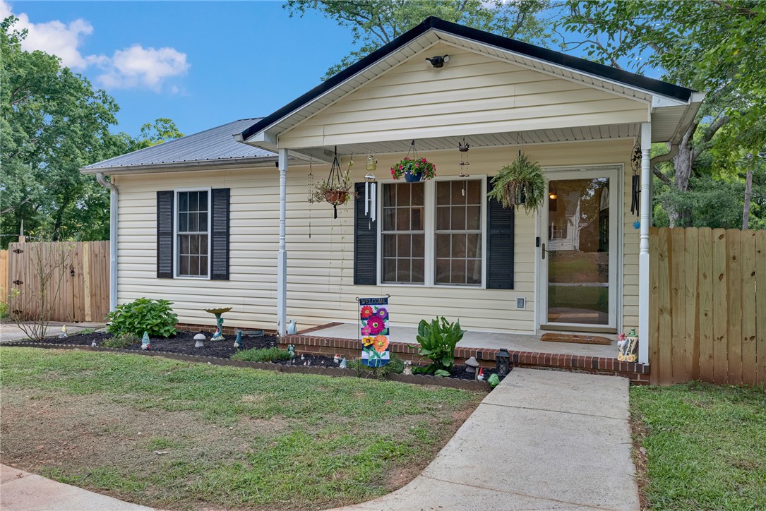 A cheerful facade with a covered porch invites, framed by a manicured lawn and vibrant garden beds.