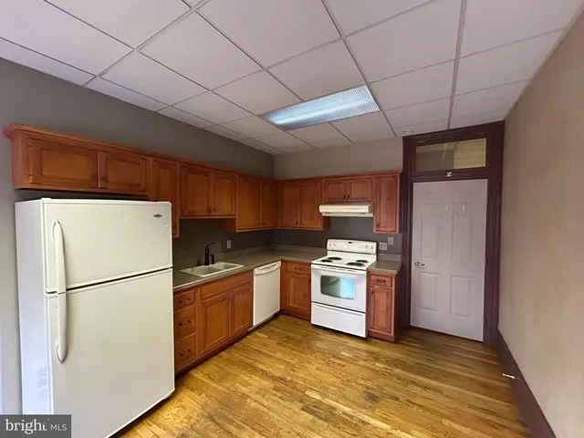 a kitchen with granite countertop a stove a sink a refrigerator wooden floor and cabinets