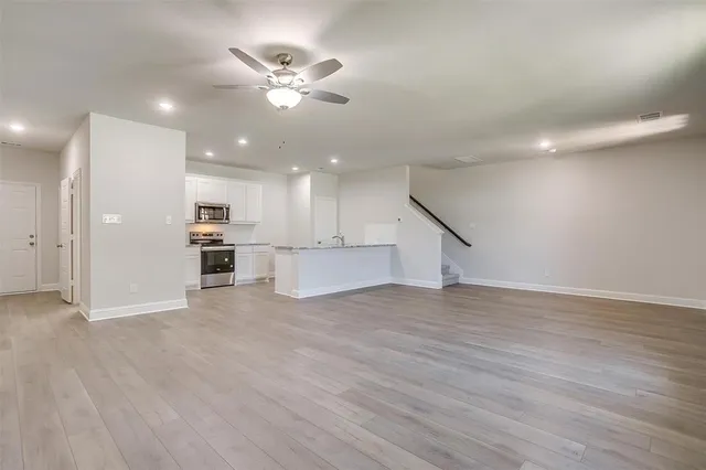 a view of an empty room with wooden floor and a ceiling fan