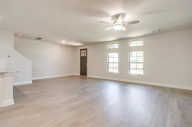 an empty room with wooden floor chandelier fan and windows