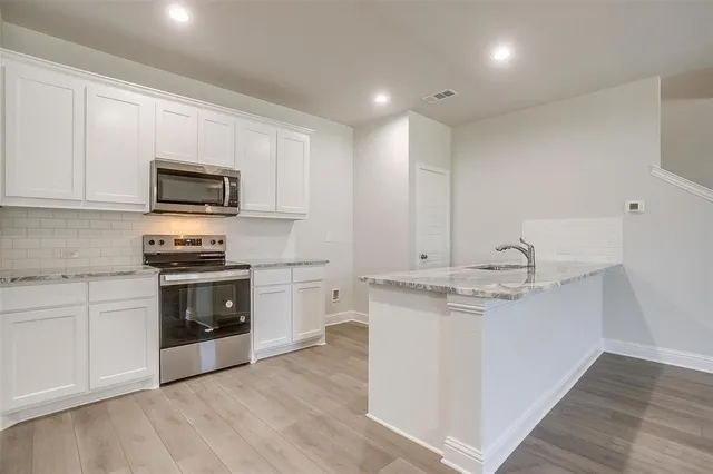 a kitchen with stainless steel appliances granite countertop a stove top oven a sink a refrigerator and white cabinets with wooden floor