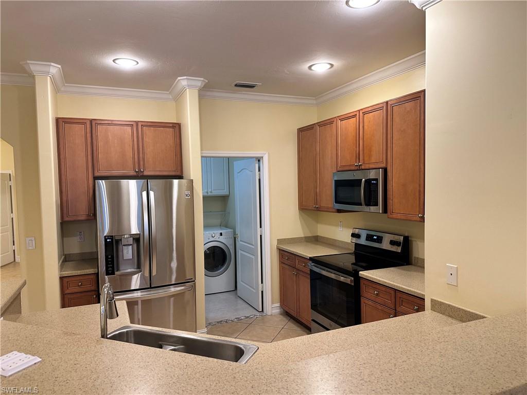 8267 Laurel Lakes Way Naples, FL 34119 - Photo 9 of 23 Kitchen featuring appliances with stainless steel finishes, brown cabinetry, ornamental molding, washer / clothes dryer, and light tile patterned floors