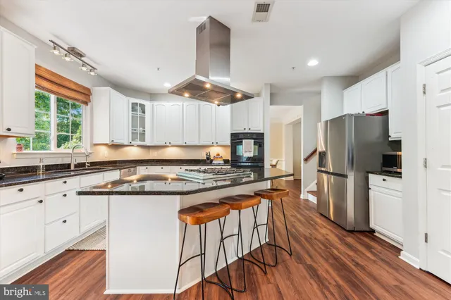 a kitchen with granite countertop a refrigerator a stove a sink cabinets and wooden floor