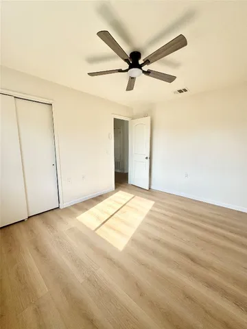 an empty room with wooden floor ceiling fan and windows