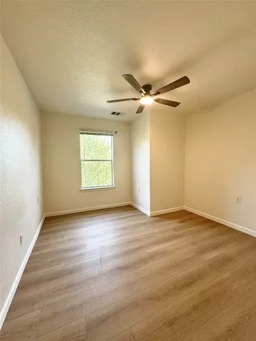 an empty room with wooden floor fan and windows