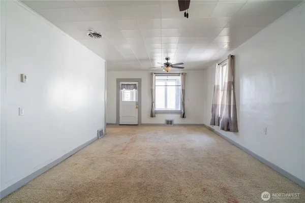 an empty room with chandelier fan and windows