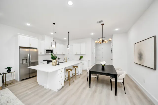 a kitchen with stainless steel appliances kitchen island a table chairs in it and white cabinets