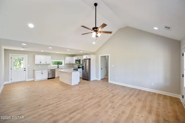 a view of an empty room and kitchen view with wooden floor