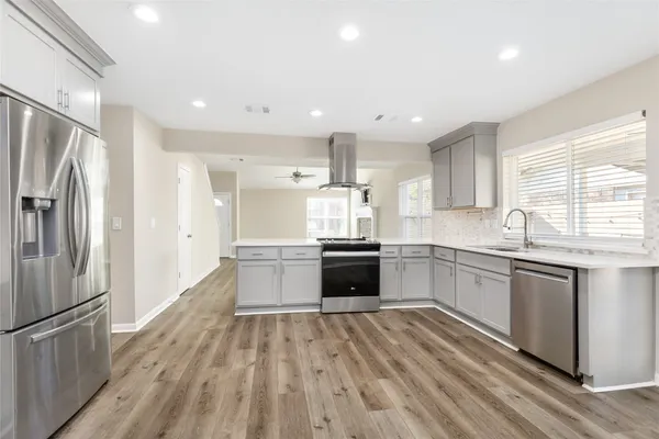 a kitchen with stainless steel appliances granite countertop a refrigerator a sink dishwasher a stove and white countertops with wooden floor