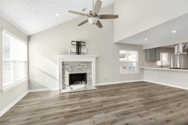 a view of an empty room with wooden floor fireplace and a ceiling fan