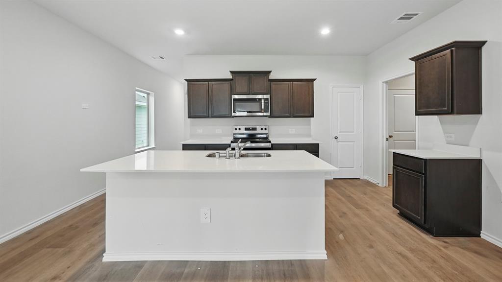 232 Pheasant Run Road Terrell, TX 75160 - Photo 27 of 36 Kitchen featuring a large island with an undermount sink, dark wood-finish cabinetry, light countertops, wood-finish flooring, and recessed lighting