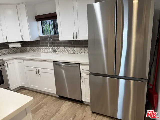 a kitchen with stainless steel appliances granite countertop a refrigerator a sink and white cabinets with wooden floor