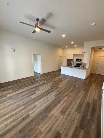 an empty room with wooden floor a ceiling fan and kitchen appliances