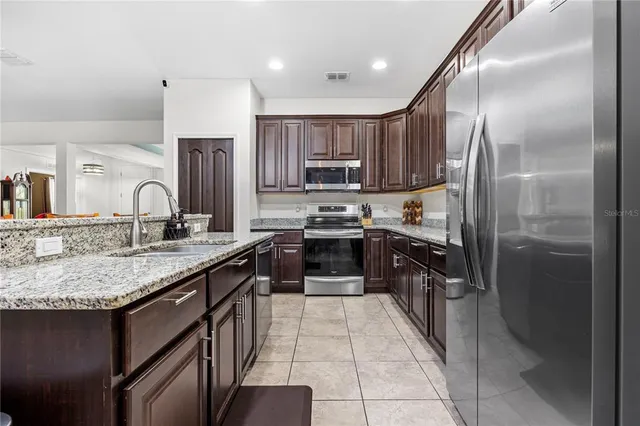 a kitchen with stainless steel appliances granite countertop a stove top oven a sink and a refrigerator with wooden floor