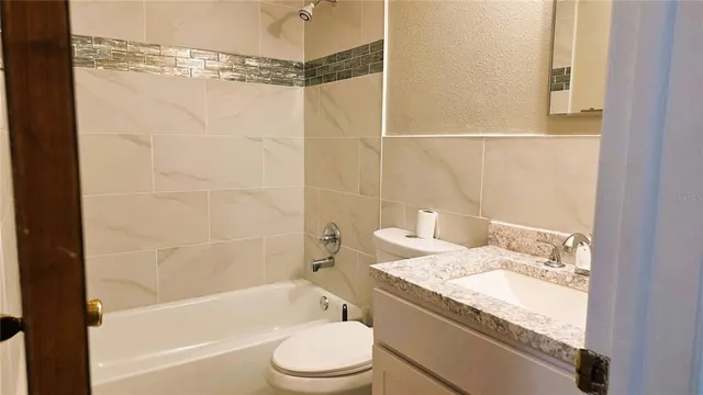 a bathroom with a granite countertop bathtub shower sink vanity and toilet