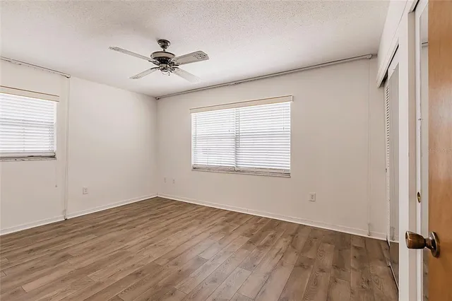 an empty room with wooden floor fan and windows