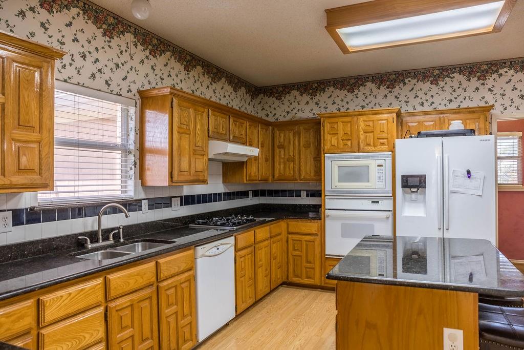 4113 Bluffpoint Road Rowlett, TX 75088 - Photo 15 of 39 Kitchen featuring dark stone counters, white appliances, brown cabinets, a center island, and light wood-style flooring
