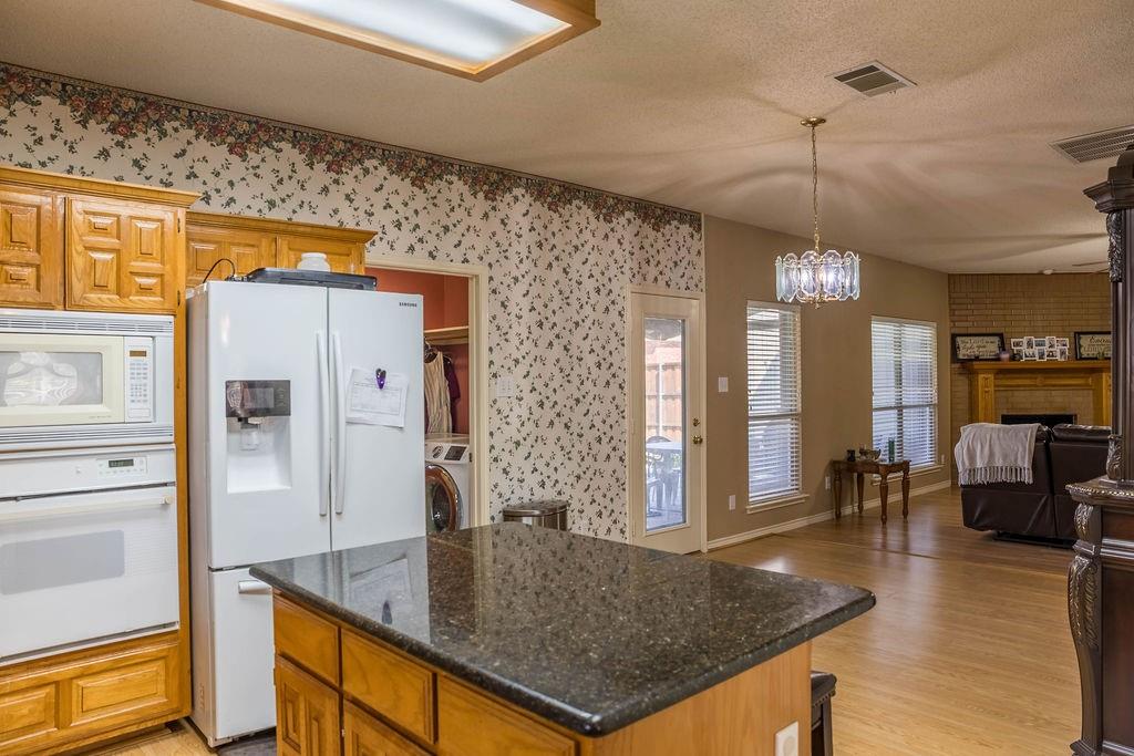 4113 Bluffpoint Road Rowlett, TX 75088 - Photo 16 of 39 Kitchen with white appliances, pendant lighting, a fireplace, light wood-style floors, and brown cabinetry