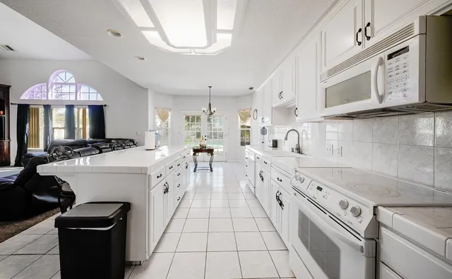a large white kitchen with a stove a sink a microwave and cabinets