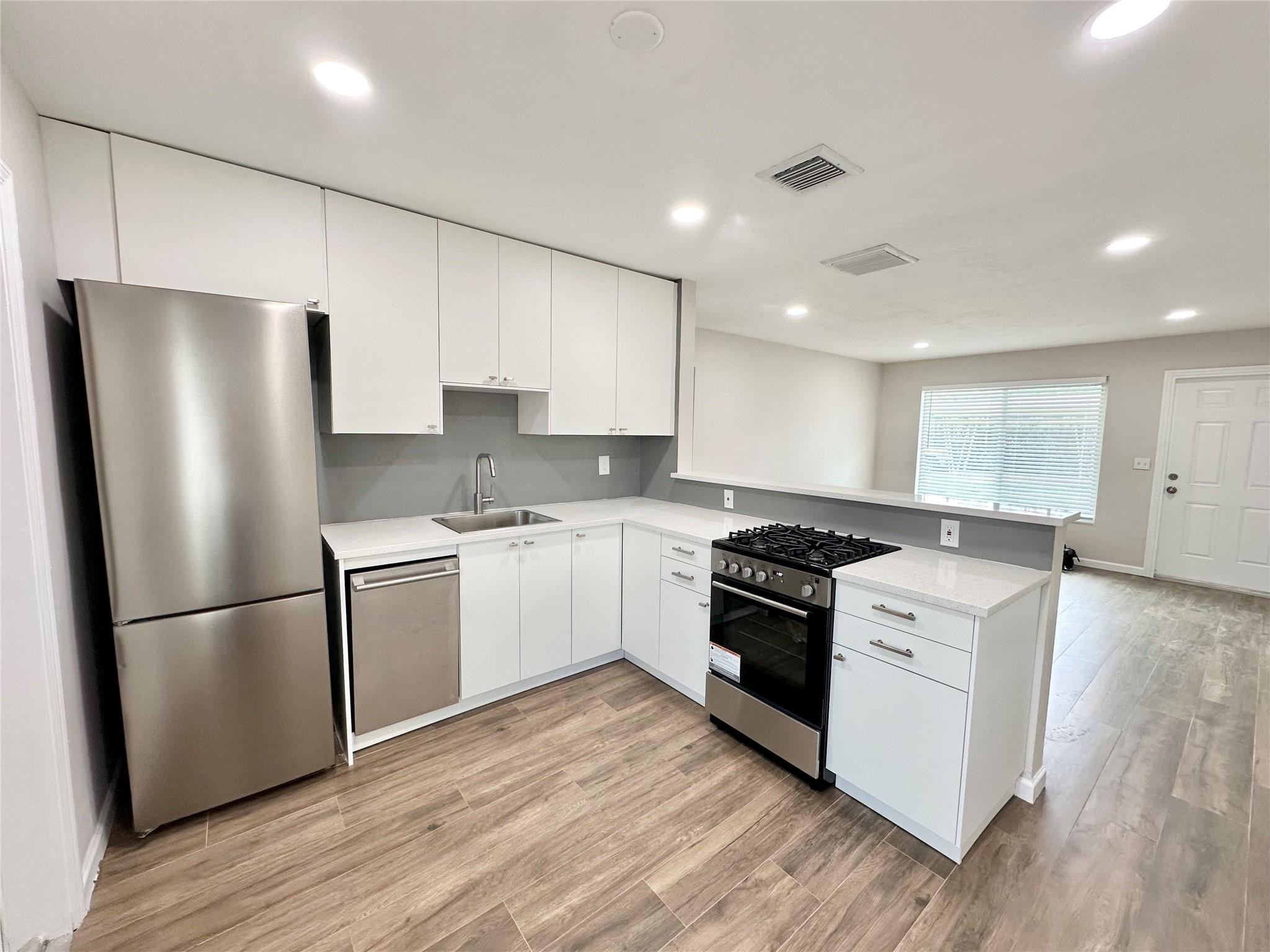 a kitchen with stainless steel appliances granite countertop a refrigerator a stove a sink and white cabinets