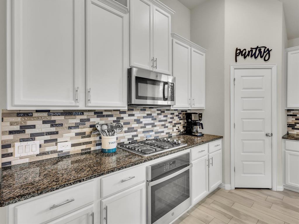 916 Monarch Lane Celina, TX 75009 - Photo 7 of 26 a kitchen with granite countertop white cabinets and stainless steel appliances