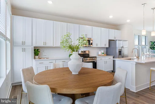 a kitchen with stainless steel appliances kitchen island granite countertop a dining table chairs and a refrigerator