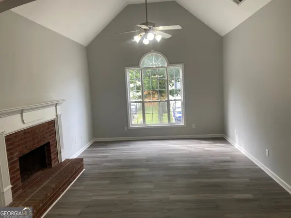 a view of an empty room with wooden floor fireplace and a window