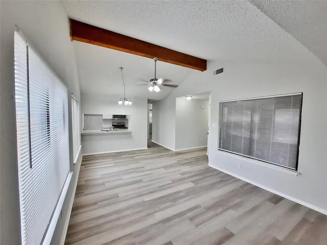 a view of an empty room with wooden floor and a kitchen