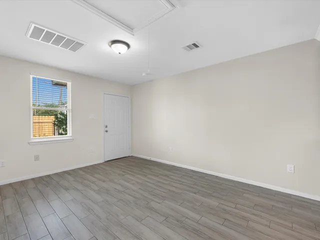 a view of an empty room with wooden floor and a window