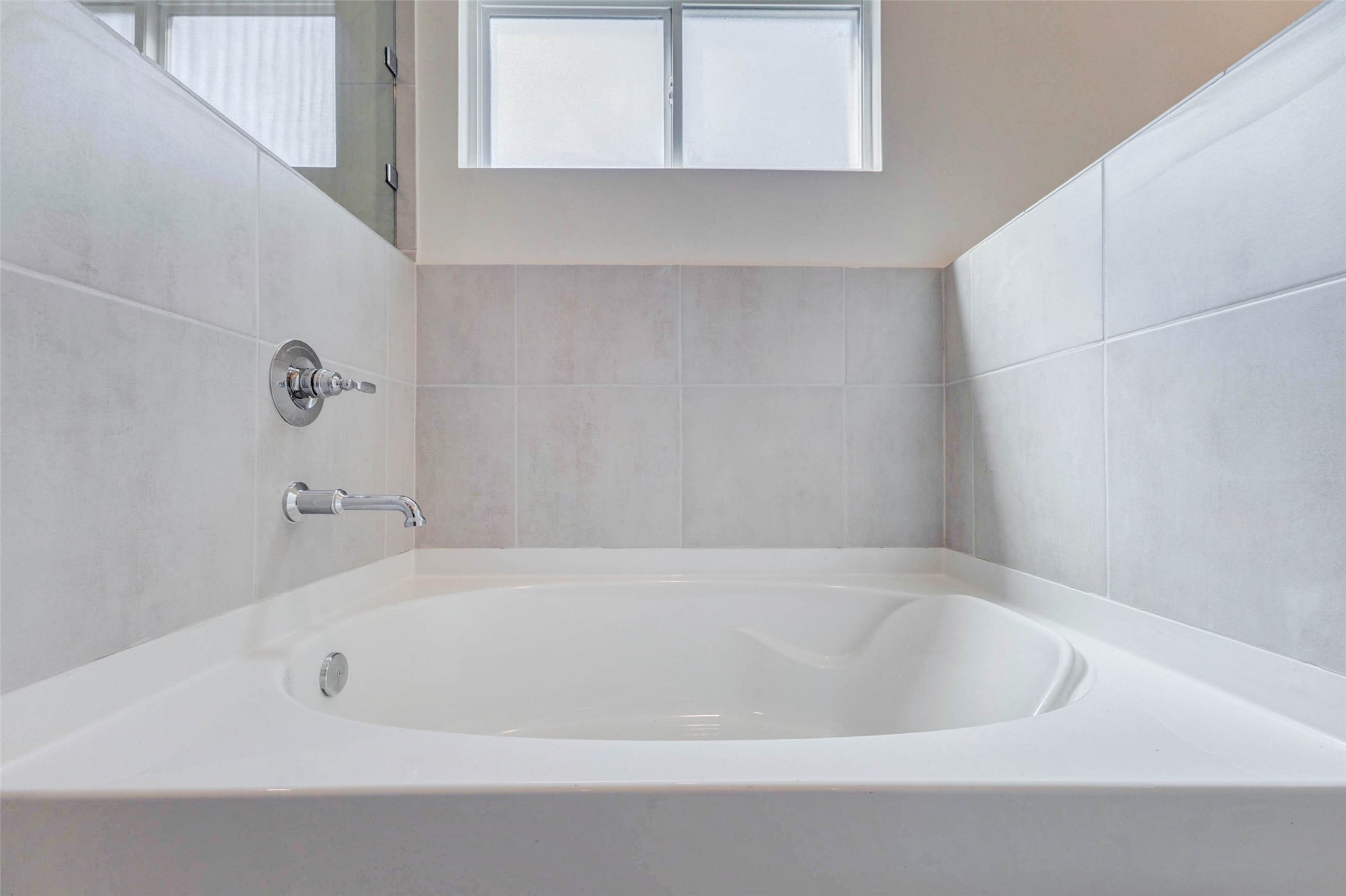 6467 Escondido Drive Rosharon, TX 77583 - Photo 23 of 32 Soaking tub detail with neutral tile surround, chrome fixtures, frosted privacy window, and a clean white tub basin. This relaxing bath area offers a quiet place to unwind, with soft natural light and simple modern finishes that complement the rest of the primary suite.