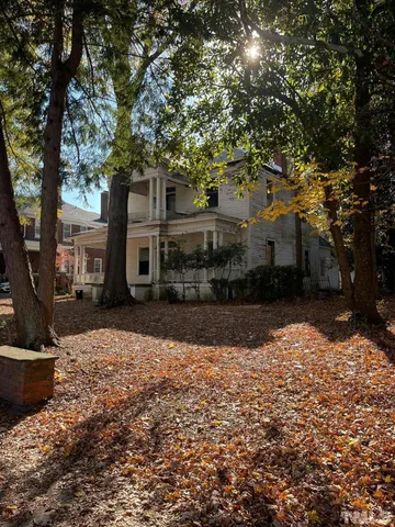 a view of a white house next to a yard with large trees