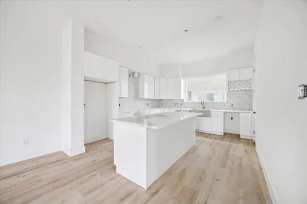 a large white kitchen with a sink dishwasher a refrigerator and white cabinets with wooden floor